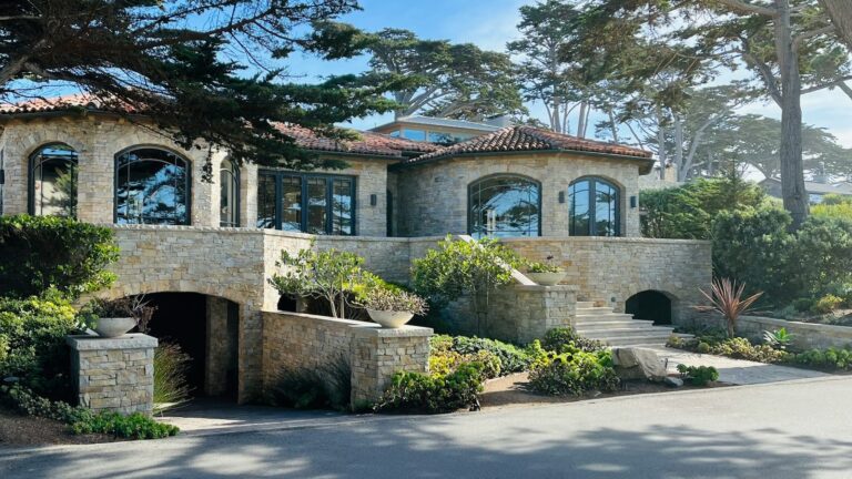 High-value California coastal home with a clay tile roof, stone masonry walls and a hardscaped, low-vegetation perimeter.